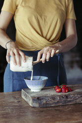 Woman preparing muesli, pouring yogurt in bowl, fresh strawberries - ALBF00343