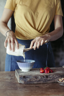 Frau bereitet Müsli zu, gießt Joghurt in eine Schüssel, frische Erdbeeren - ALBF00344