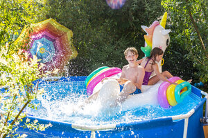 Bruder und Schwester mit übergroßem Einhorn-Schwimmspielzeug im Planschbecken - SARF03778