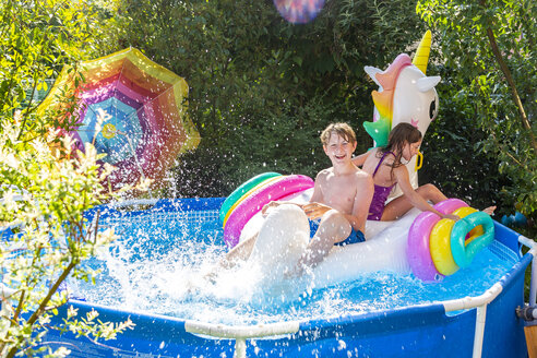 Brother and sister with oversized unicorn swim toy in paddling pool - SARF03778