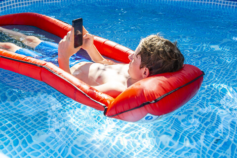 Boy floating on water in swimming pool using smartphone stock photo