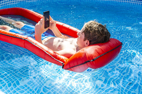 Junge schwimmt im Schwimmbad auf dem Wasser und benutzt sein Smartphone - SARF03779