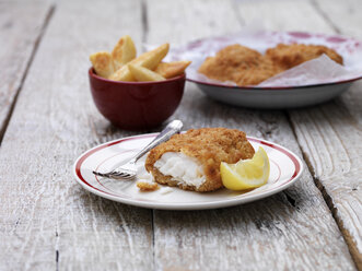 Panierter Kabeljau mit einer Schüssel Pommes frites auf einem Holztisch - CUF28298