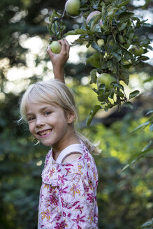 Porträt eines lachenden Mädchens, das einen Apfel vom Baum pflückt - JFEF00876