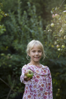 Porträt eines lächelnden Mädchens, das einen Apfel anbietet - JFEF00878