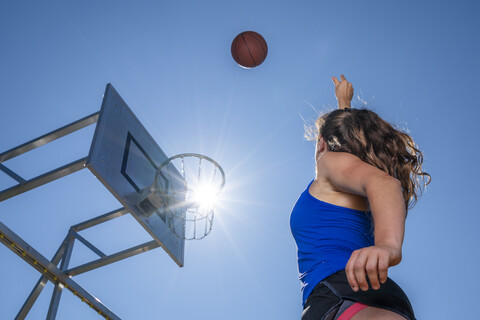 Junge Frau spielt Basketball, gegen die Sonne, lizenzfreies Stockfoto