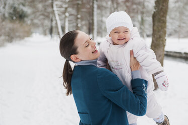 Porträt eines glücklichen kleinen Mädchens, das mit seiner Mutter in einer verschneiten Landschaft Spaß hat - DIGF04570