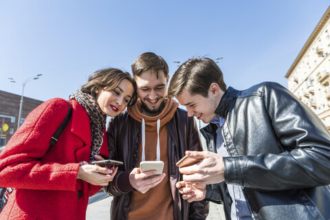 Russland, Moskau, drei Freunde schauen gemeinsam auf ein Smartphone, lizenzfreies Stockfoto