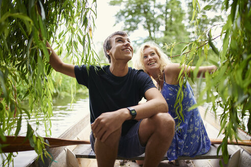 Young couple touching willow tree foliage from rowing boat on rural river - CUF28607