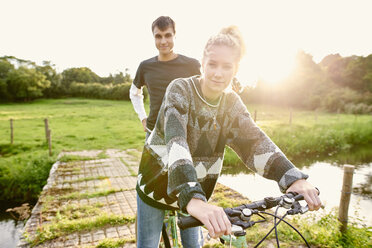 Porträt eines jungen Paares auf einem Fahrrad an einem Flusssteg - CUF28613
