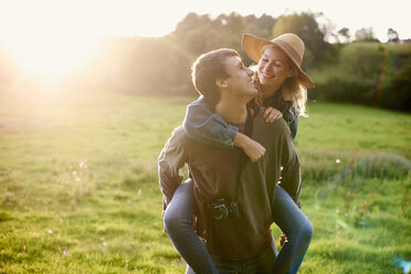 Young man giving girlfriend a piggyback in rural field - CUF28616