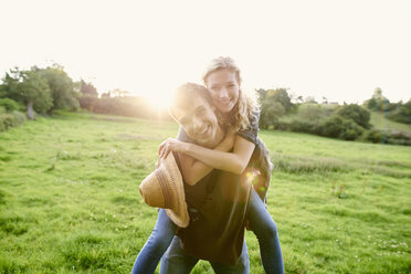 Portrait of young man giving girlfriend a piggyback in rural field - CUF28619