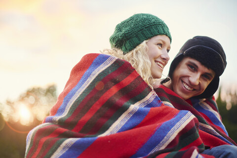 Porträt eines romantischen jungen Campingpaares, eingewickelt in eine Decke, lizenzfreies Stockfoto