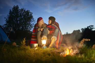 Junges Campingpaar am Lagerfeuer in der Abenddämmerung - CUF28631