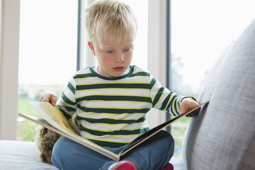 Junge sitzt auf Sofa und liest ein Buch - CUF28634