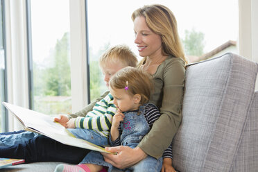 Mutter und zwei kleine Kinder sitzen auf dem Sofa und lesen ein Buch - CUF28635