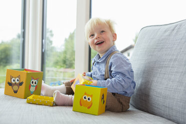 Porträt eines glücklichen männlichen Kleinkindes, das auf dem Sofa mit Bauklötzen spielt - CUF28637