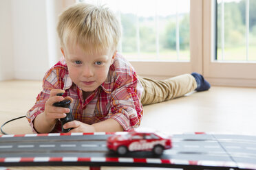 Junge spielt mit Spielzeug-Rennauto auf dem Boden im Wohnzimmer - CUF28640