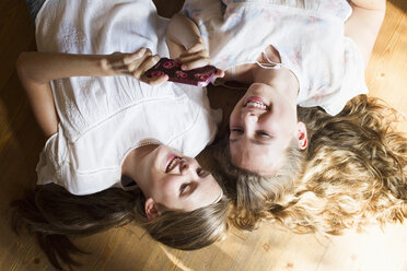 Two teenage girls lying on wooden floor reading smartphone texts - CUF28642