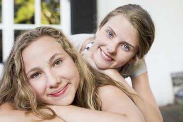 Portrait of two teenage girls lying on patio - CUF28652