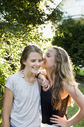 Two teenage girls whispering in garden - CUF28653