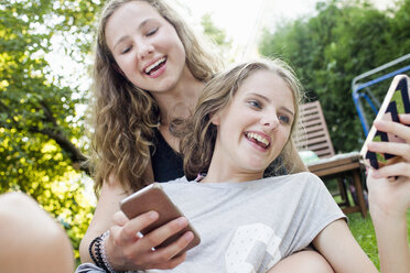 Two teenage girls reading smartphone texts in garden - CUF28654