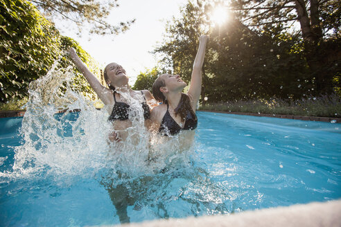 Zwei Mädchen im Teenageralter springen mit erhobenen Armen in ein Schwimmbecken - CUF28658