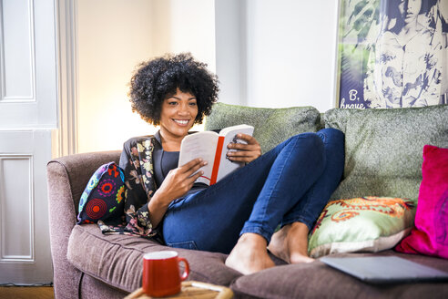 Reife Frau entspannt sich auf dem Wohnzimmersofa und liest ein Buch - CUF28683