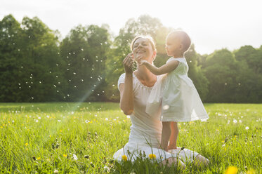Mother and daughter with blowball on meadow in summer - DIGF04598