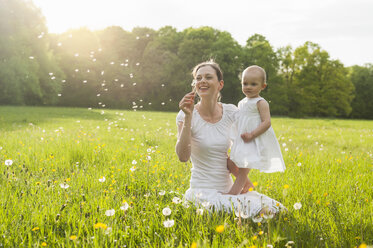 Mother and daughter with blowball on meadow in summer - DIGF04599