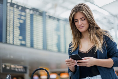 Junge Frau benutzt ein Handy an der Abflugtafel und schaut sich um - DIGF04612