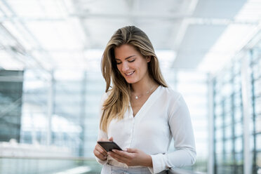 Lächelnde junge Frau steht am Geländer und benutzt ein Mobiltelefon - DIGF04617