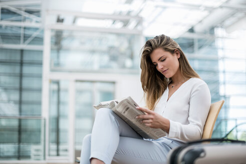 Junge Geschäftsfrau sitzt mit Koffer im Freien und liest Zeitung - DIGF04619