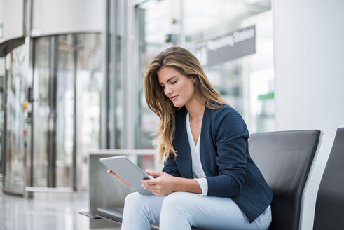 Junge Geschäftsfrau sitzt im Wartebereich und benutzt ein Tablet - DIGF04624