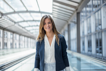Portrait of smiling young businesswoman on moving walkway - DIGF04627
