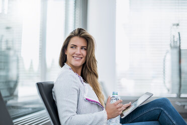 Lächelnde junge Geschäftsfrau, die im Wartebereich sitzt und ein Tablet benutzt - DIGF04638