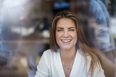 Porträt einer glücklichen jungen Frau hinter einer Fensterscheibe - DIGF04647