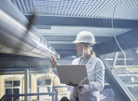 Technikerin bei der Arbeit an Rohrleitungen, mit Laptop, lizenzfreies Stockfoto