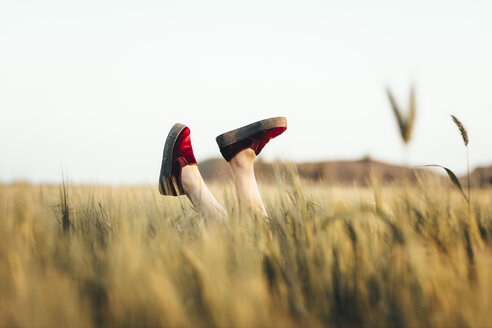 Woman lying in cornfield, kicking legs with red shoes - OCAF00285