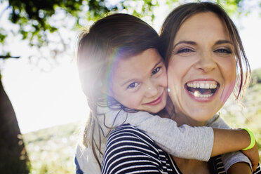 Portrait of mature woman giving daughter piggy back in sunlit park - CUF29089