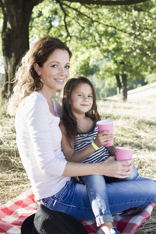 Porträt einer reifen Frau und ihrer Tochter, die beim Picknick im Park aus Pappbechern trinken, lizenzfreies Stockfoto