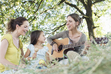 Ältere Frau spielt Akustikgitarre für Freund und Tochter im Park - CUF29098