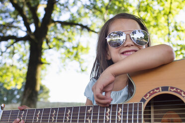 Mädchen mit Sonnenbrille posiert mit akustischer Gitarre im Park - CUF29100