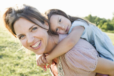 Mature woman giving daughter piggy back ride in park - CUF29111