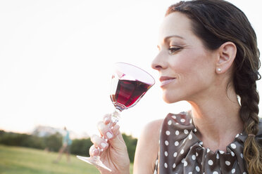 Reife Frau trinkt ein Glas Rotwein im Park - CUF29119
