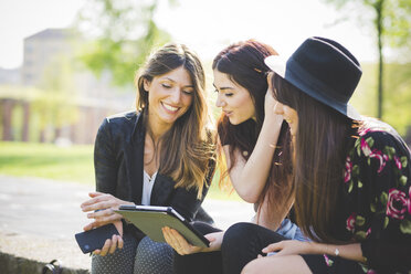 Three young female friends sharing update on digital tablet in park - CUF29136