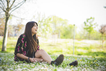Young woman sitting on park grass listening to earphones - CUF29138