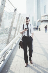 Businessman reading smartphone text update whilst walking on footbridge - CUF29166