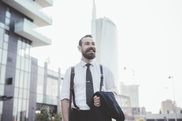 Stylish bearded businessman carrying jacket walking in city - CUF29172
