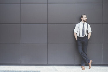 Stylish businessman with hands in pockets leaning against office wall - CUF29175